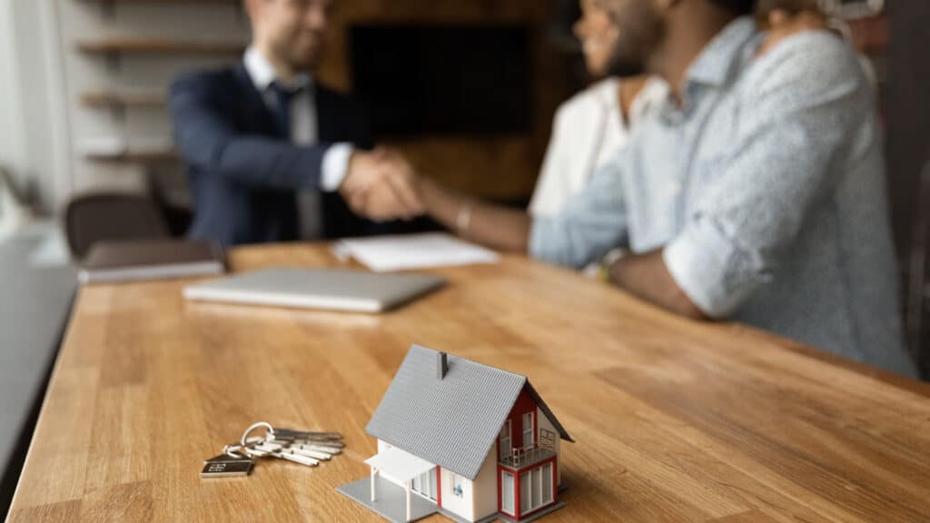 Using a 1031 exchange on a primary residence is illustrated by a couple shaking hands with a real estate agent while closing the sale of their house.
