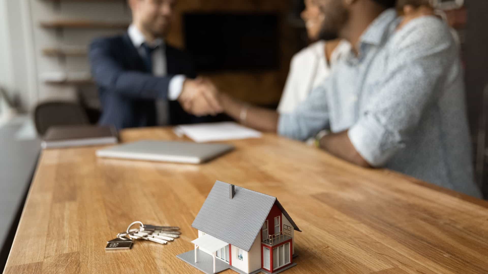 Using a 1031 exchange on a primary residence is illustrated by a couple shaking hands with a real estate agent while closing the sale of their house.